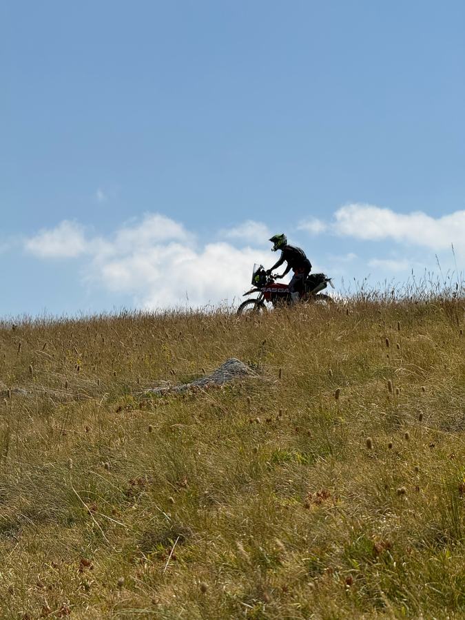 Fahrer auf beladenem Motorrad auf einem Grasrücken vor dem Himmel