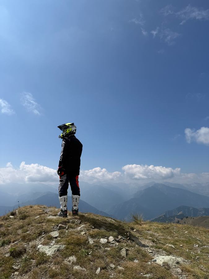 Fahrer steht auf einem Gipfel und blickt über gestaffelte Bergketten