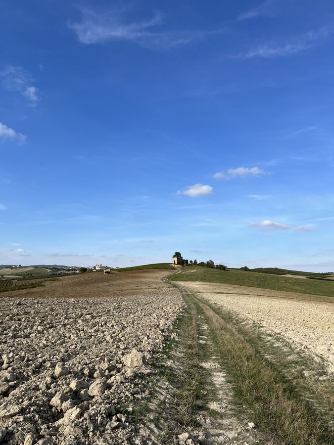 Weg durch gepflügte Felder hinauf zu einer kleinen Kapelle auf einem Hügel